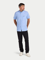 Man wearing a light blue short-sleeve shirt and black pants on a white background