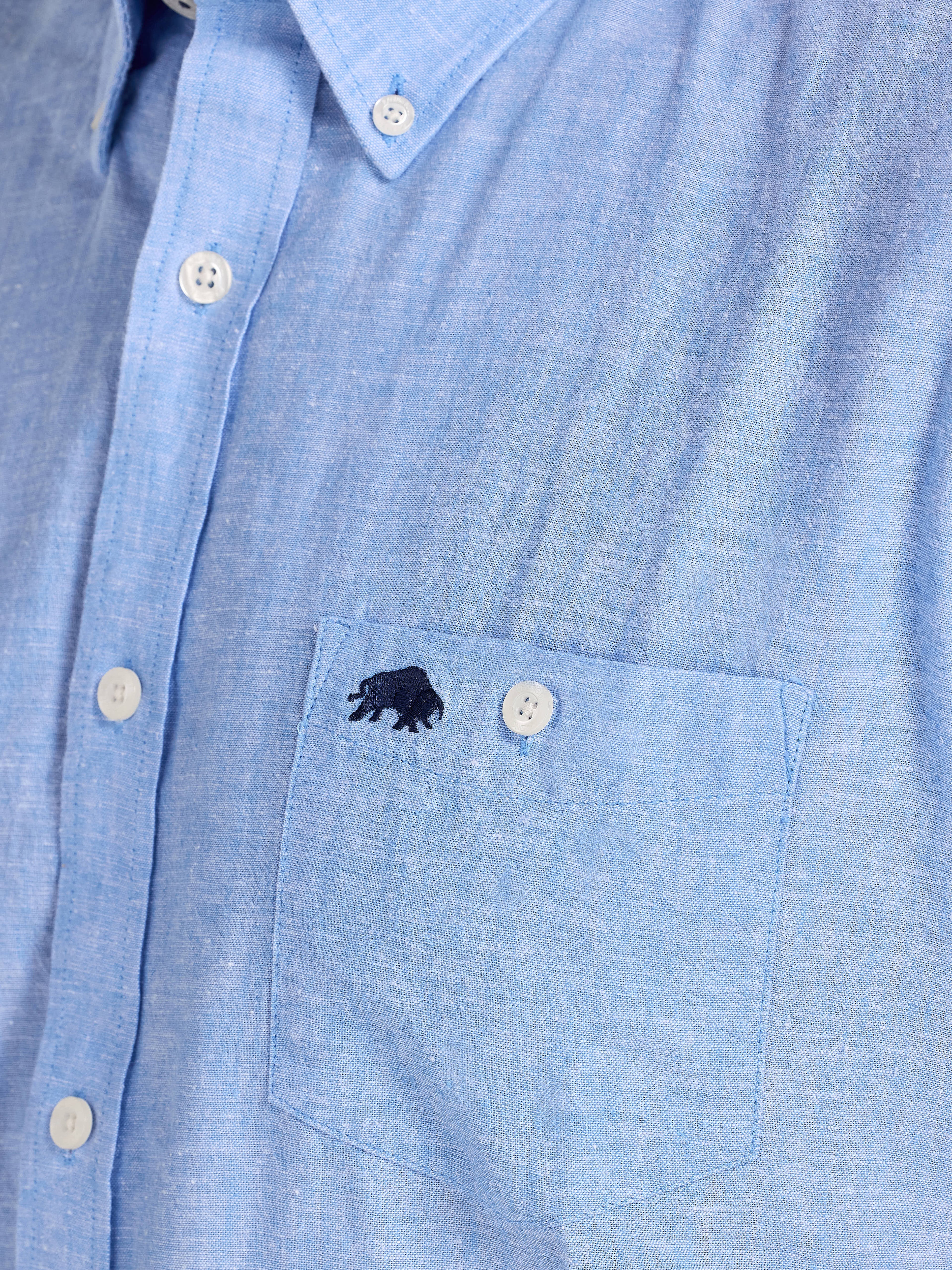 Close-up of a blue shirt with a small logo on the chest pocket.