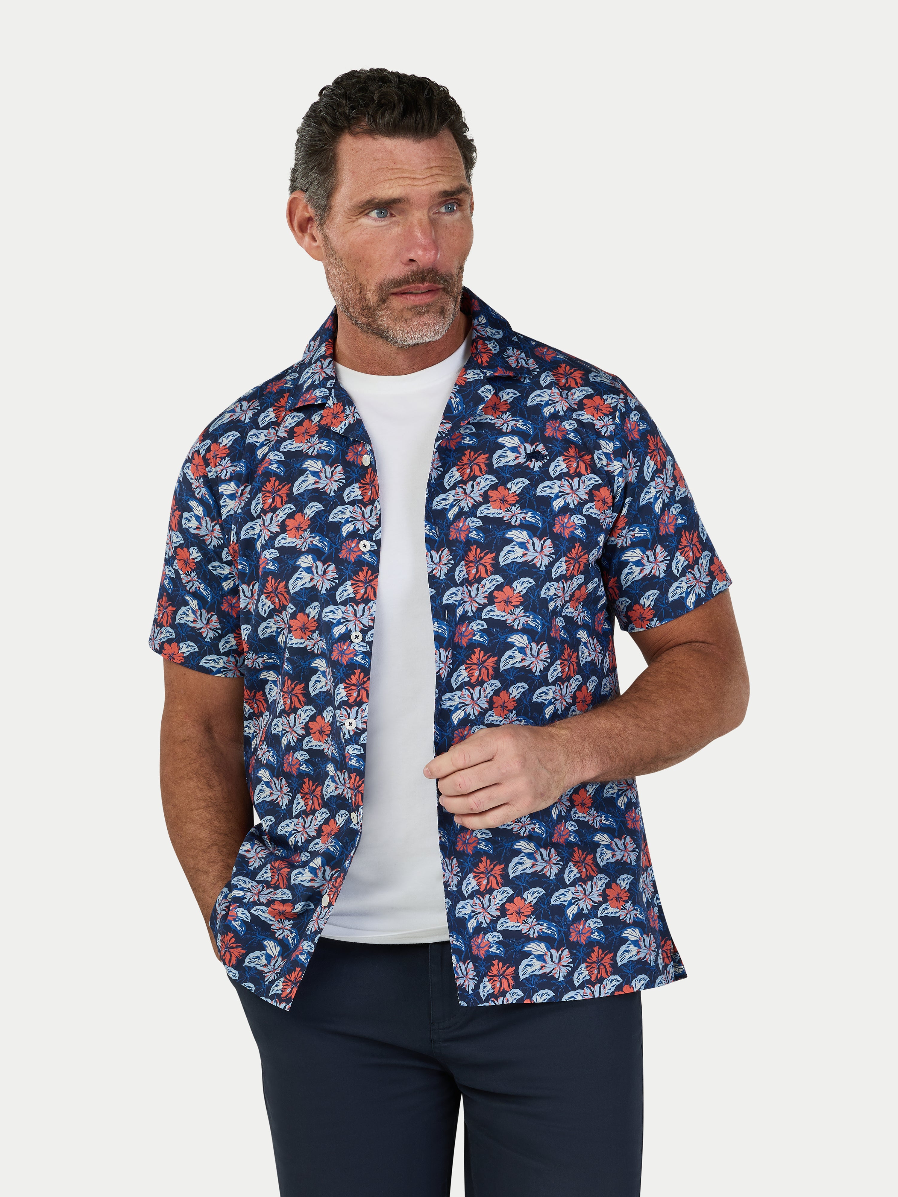 Man wearing a blue floral patterned shirt over a white t-shirt on a light gray background