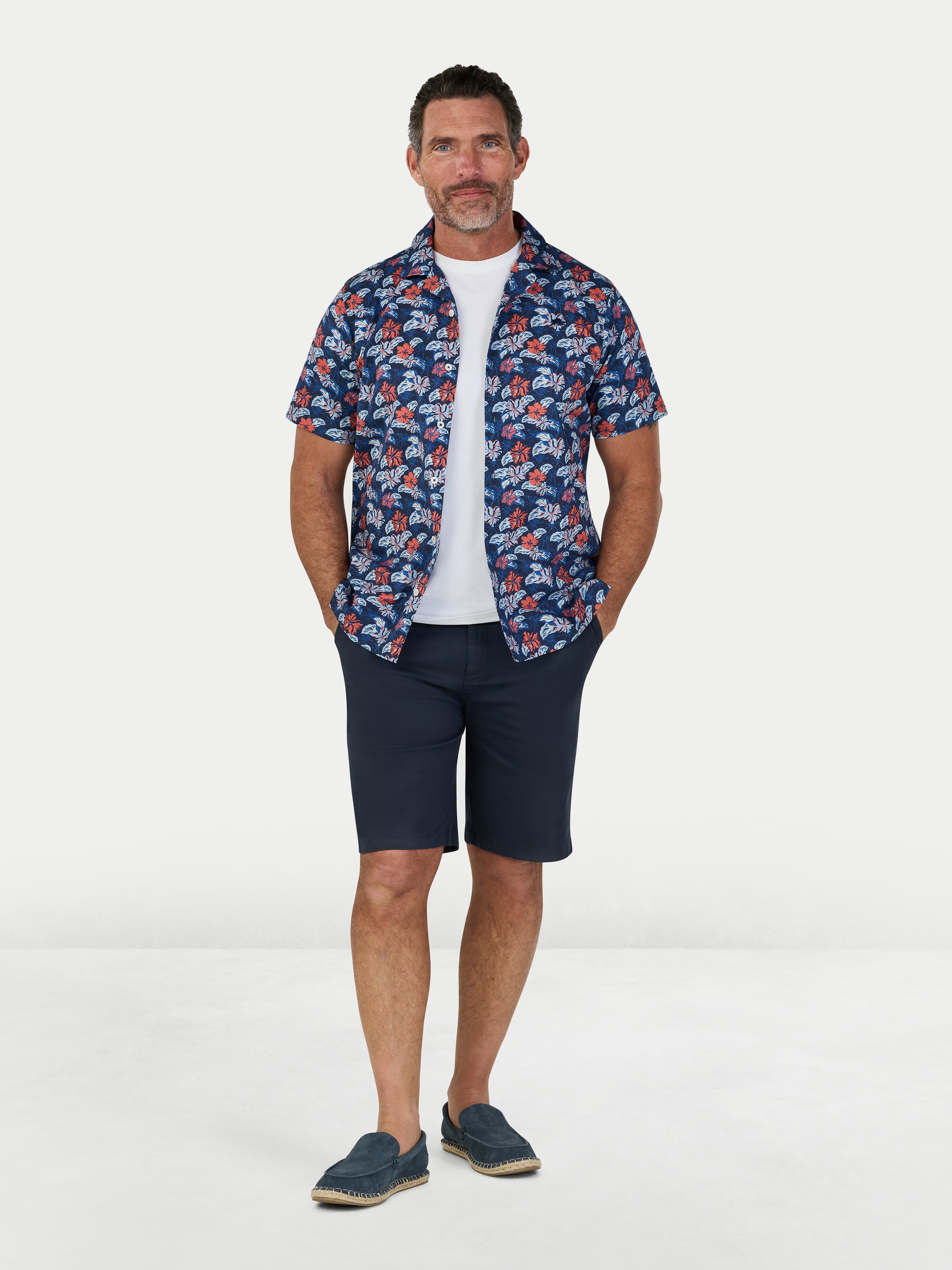 Man wearing a patterned shirt, white t-shirt, and navy shorts on a white background