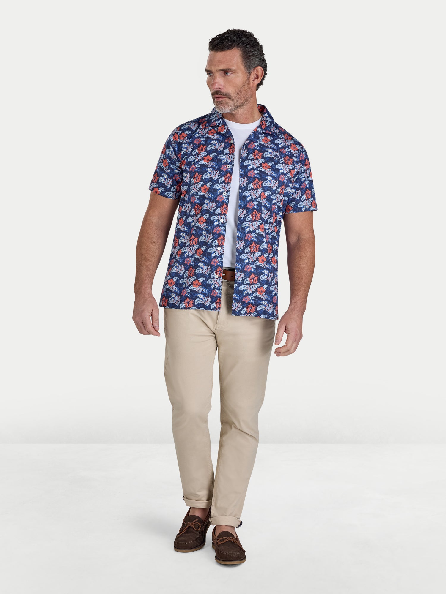 Man wearing a patterned shirt and beige pants on a white background