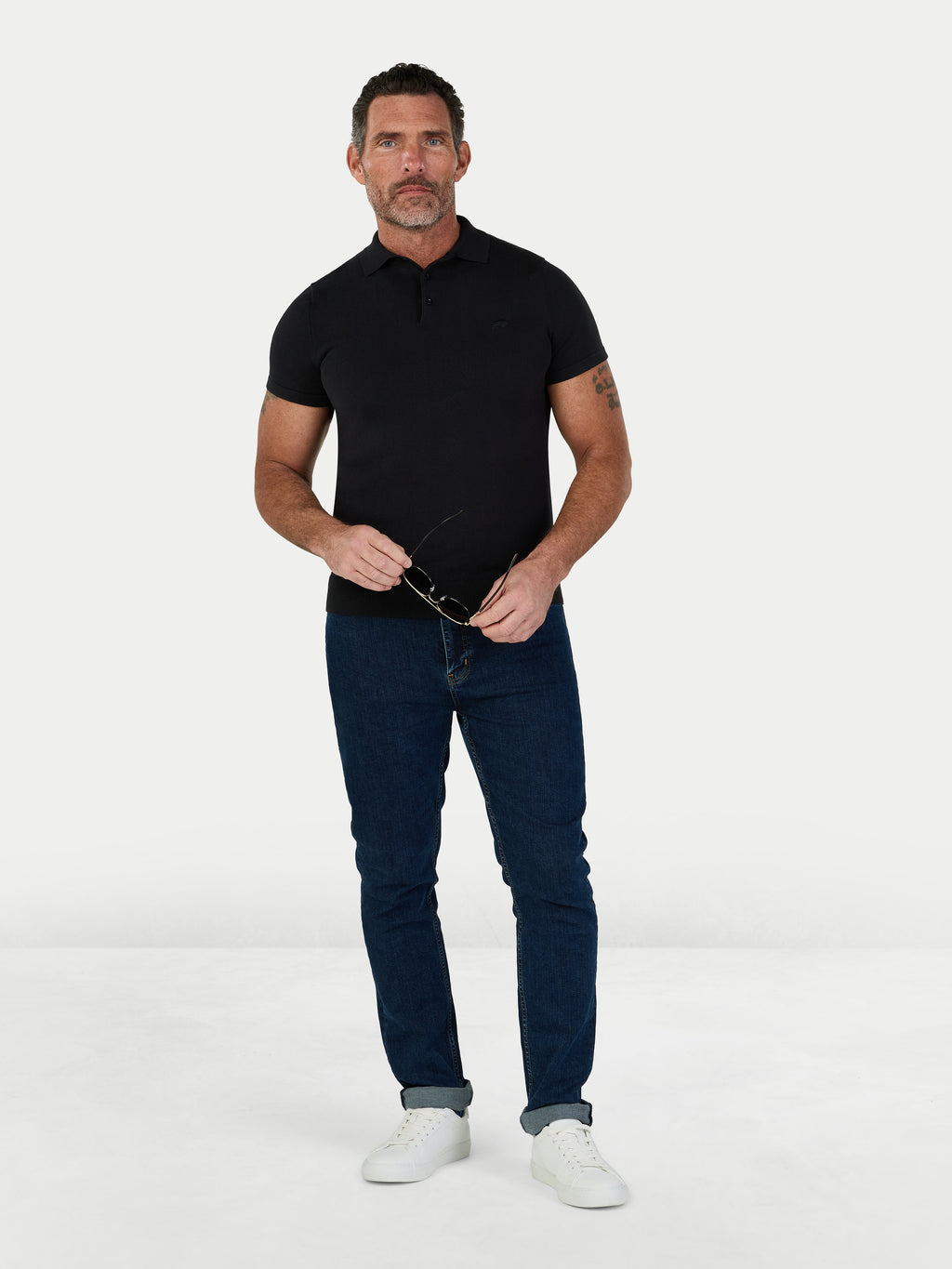 Man wearing a black polo shirt and dark blue jeans on a white background