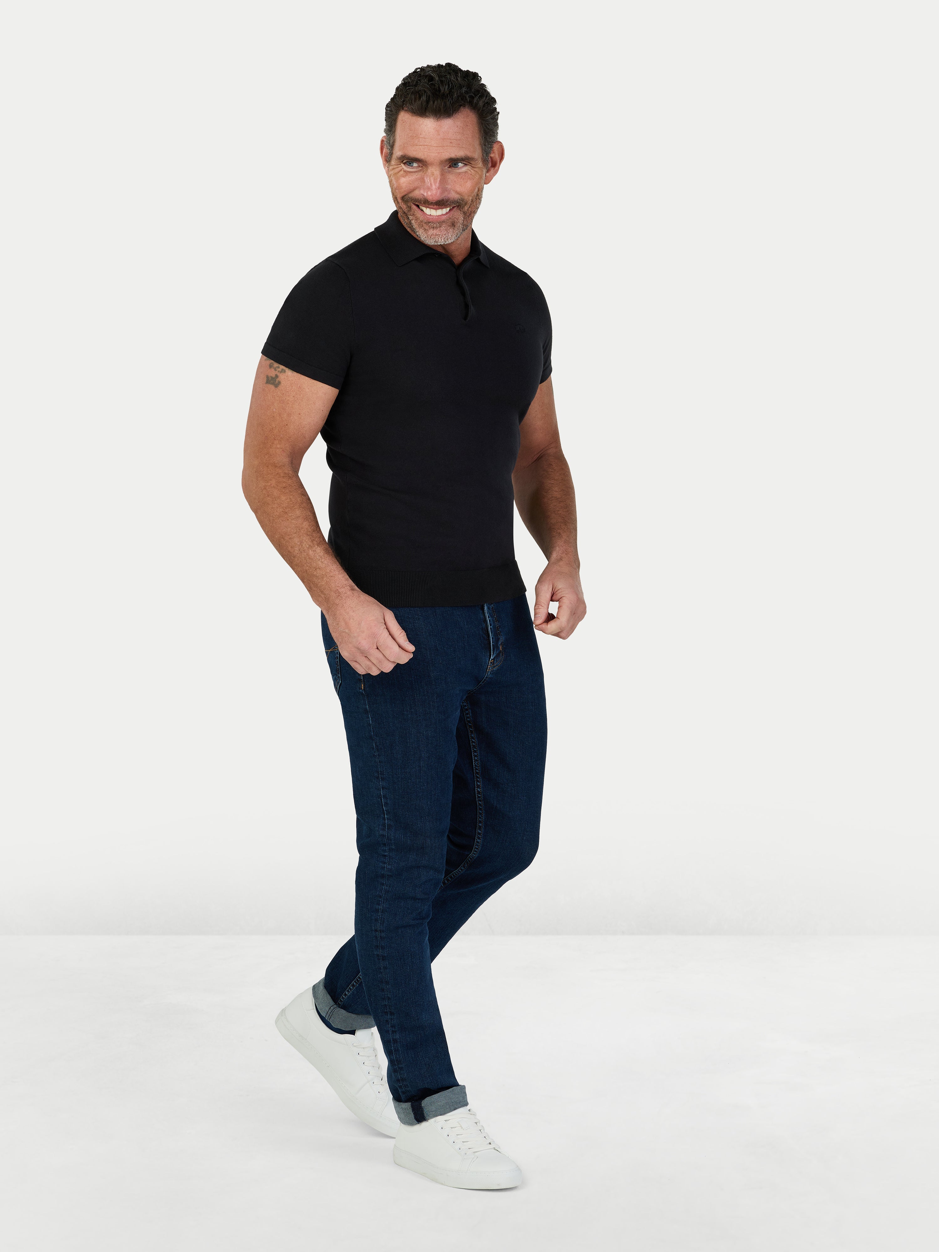 Man wearing a black polo shirt and blue jeans on a white background