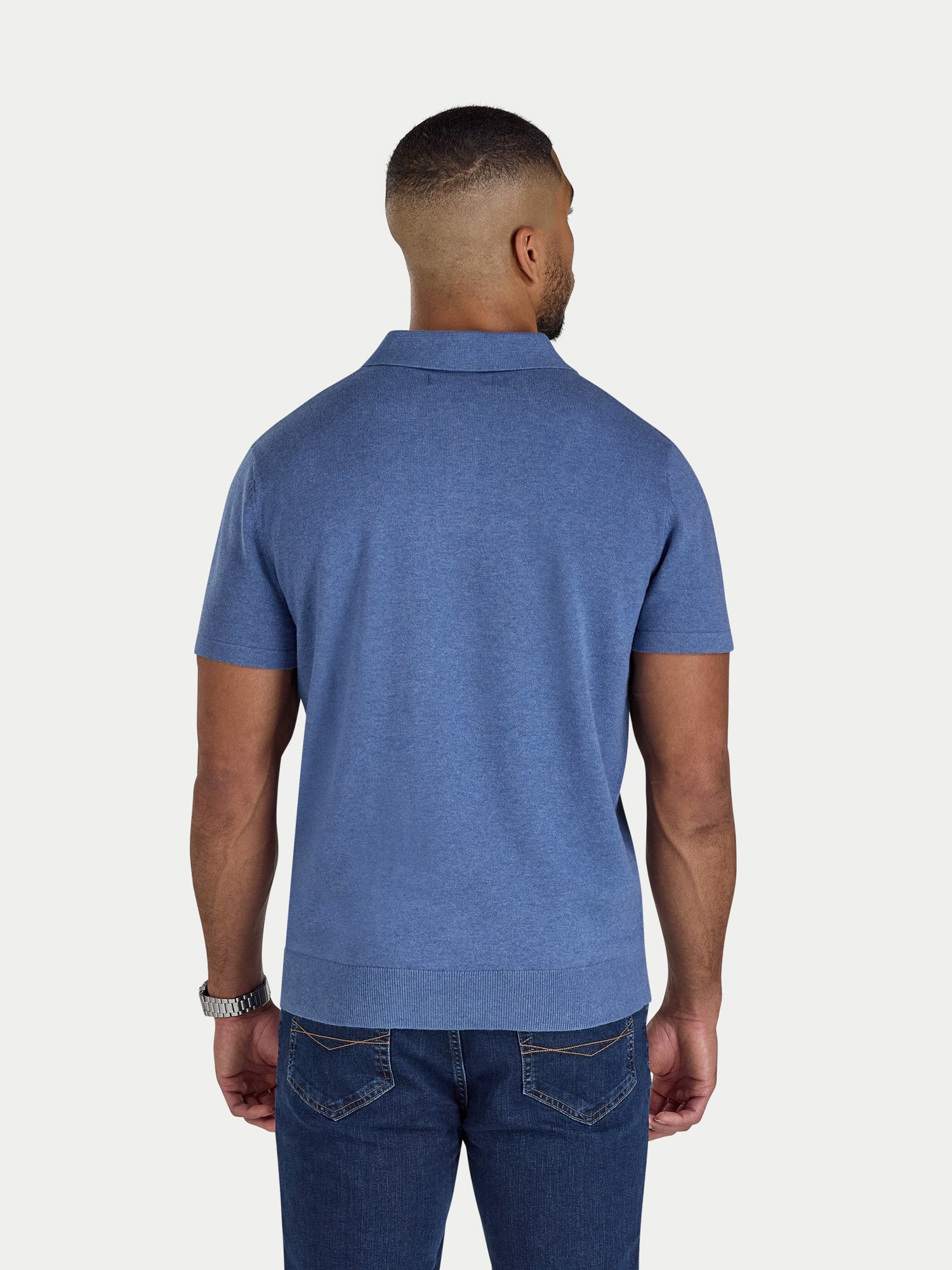 Man wearing a blue polo shirt and jeans on a white background