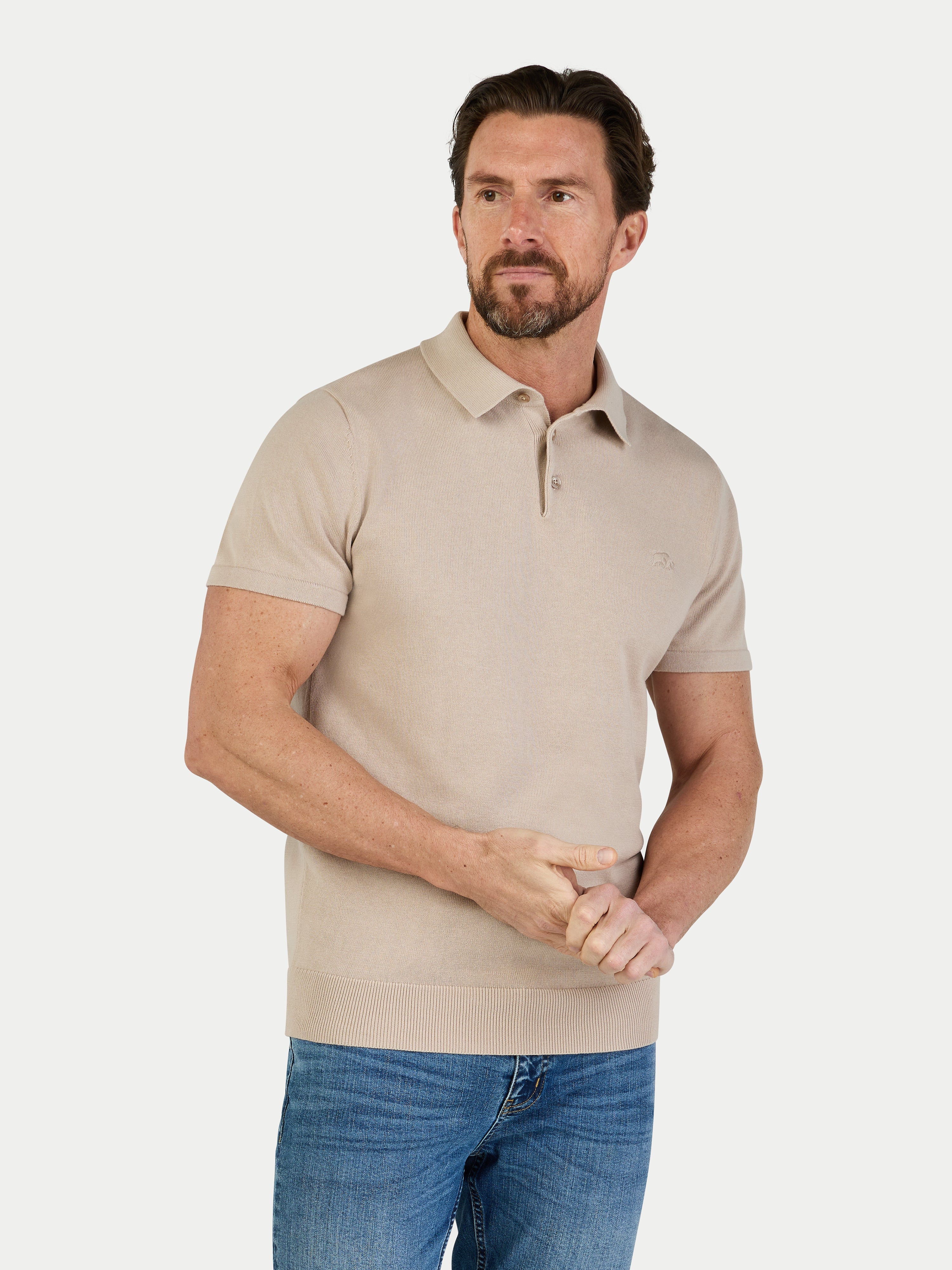 Man wearing a beige polo shirt and blue jeans on a white background