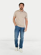 Man wearing a beige polo shirt and blue jeans on a white background