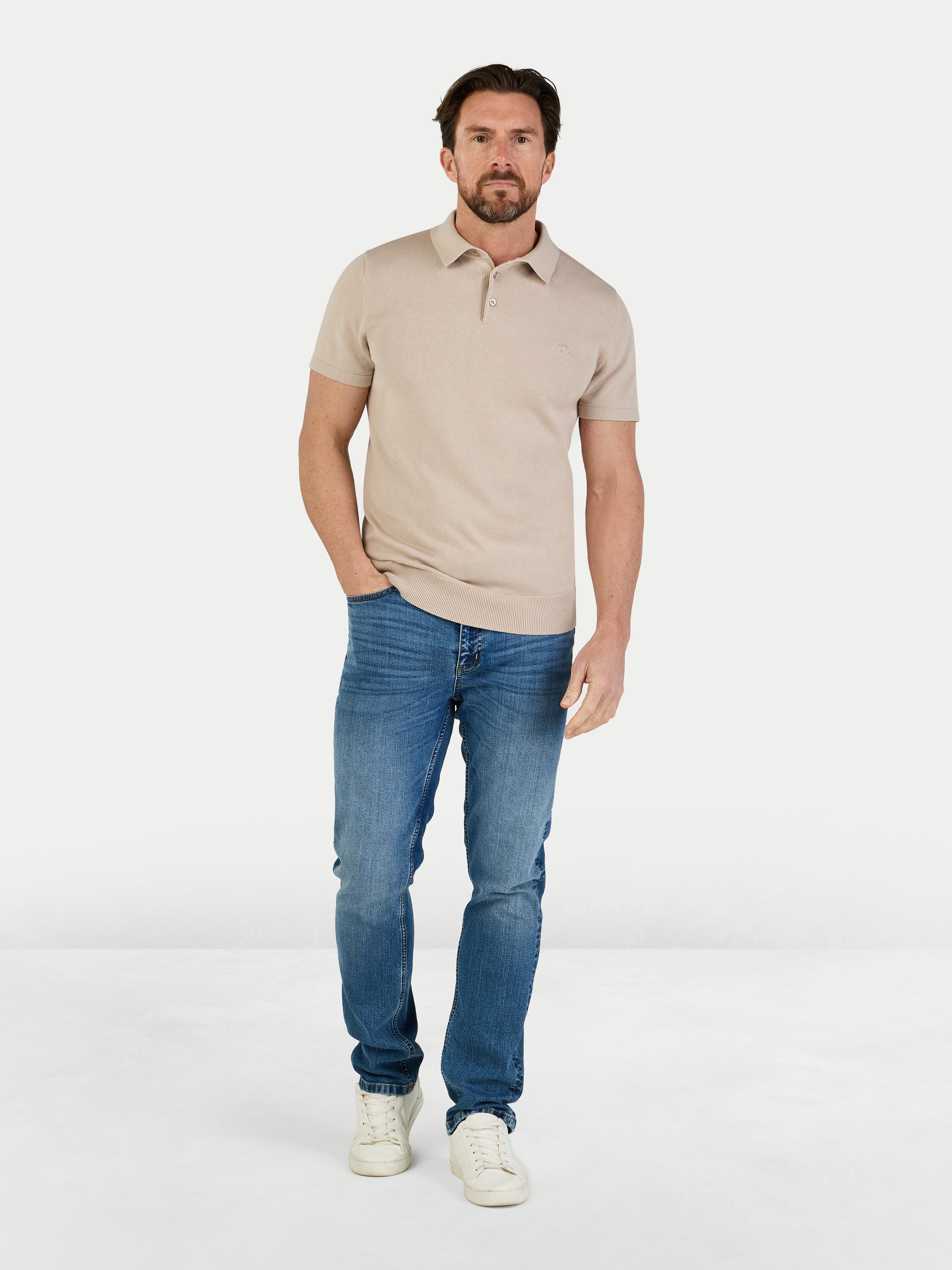 Man wearing a beige polo shirt and blue jeans on a white background