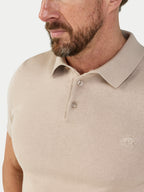 Man wearing a beige polo shirt with a brand logo on a light gray background