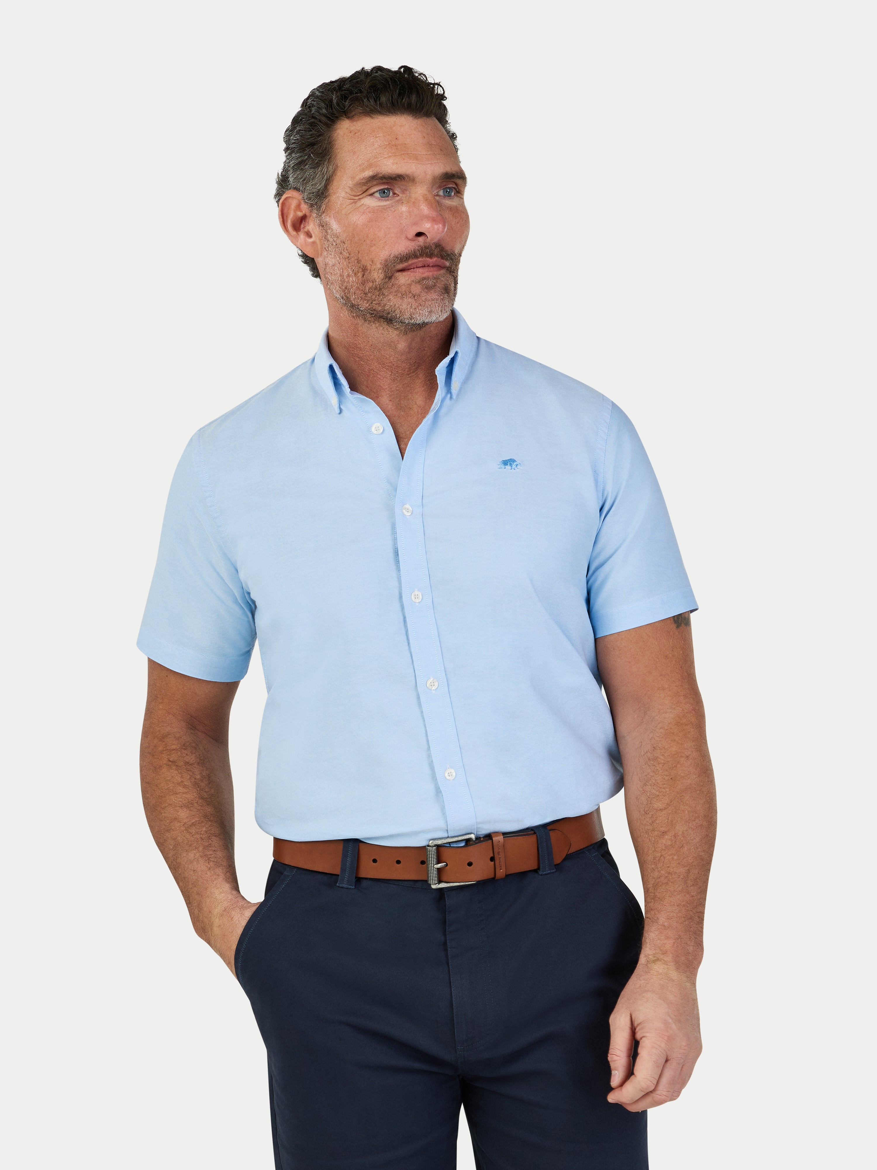 Man wearing a light blue short-sleeve shirt and navy pants on a white background