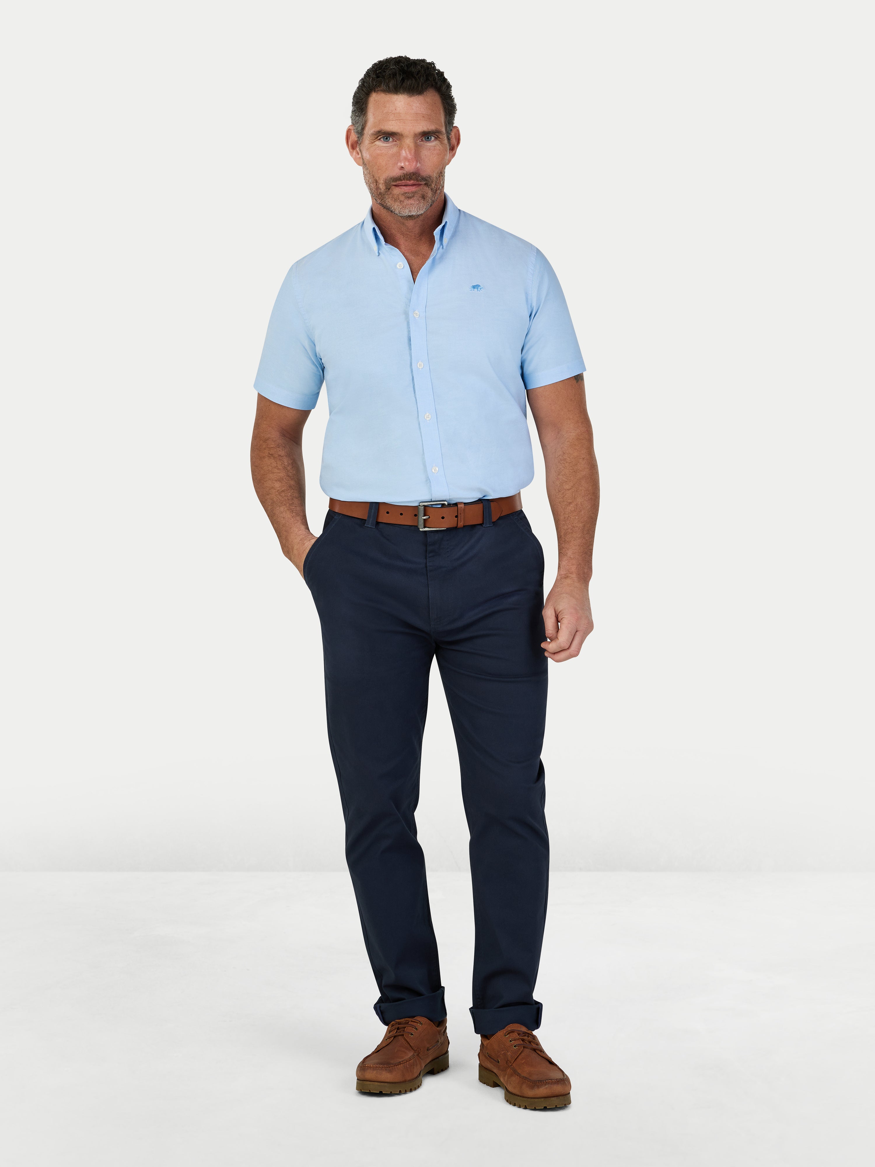 Man wearing a light blue shirt, navy pants, and brown shoes on a white background