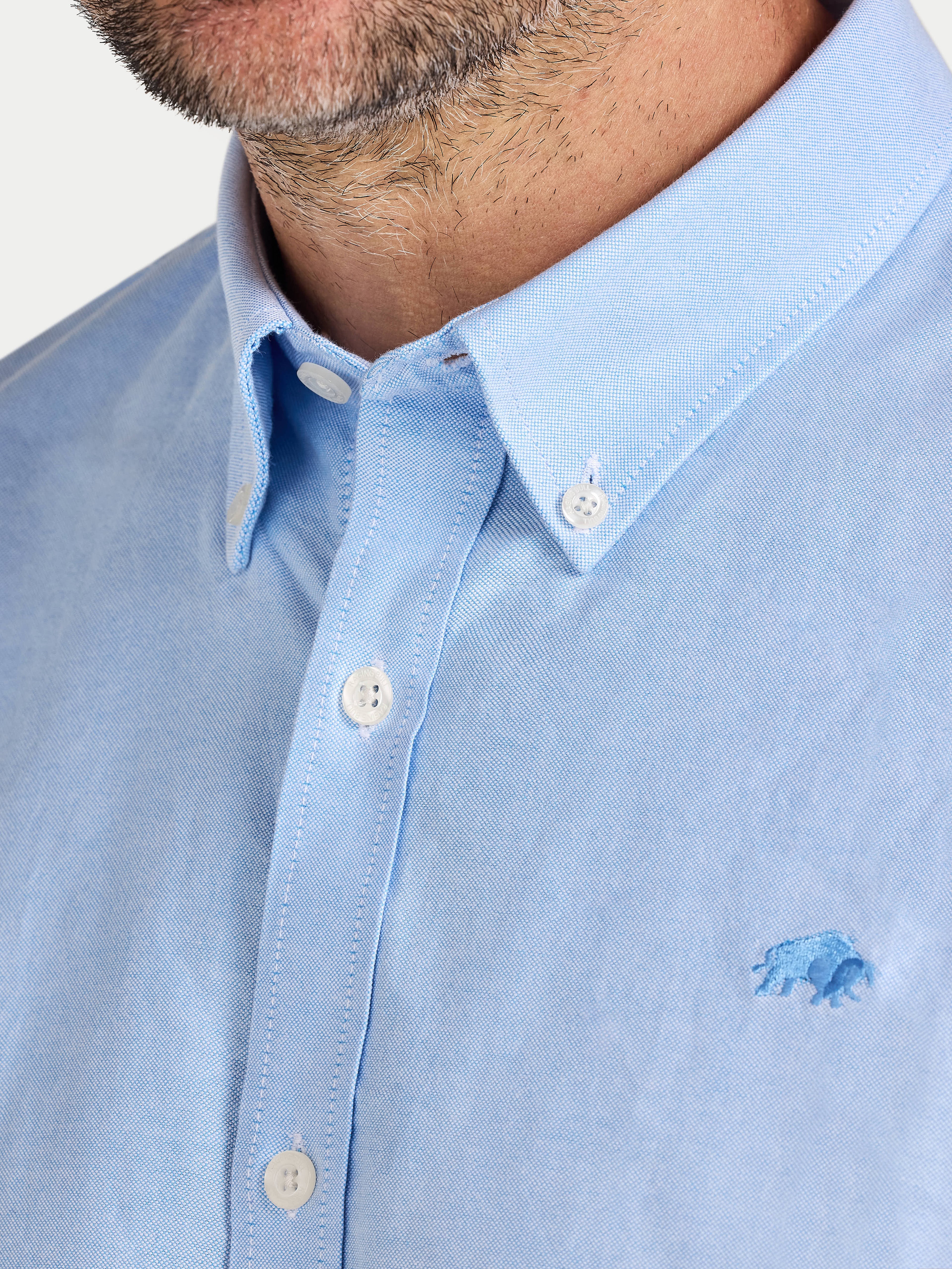 Close-up of a light blue shirt with a small logo on a white background