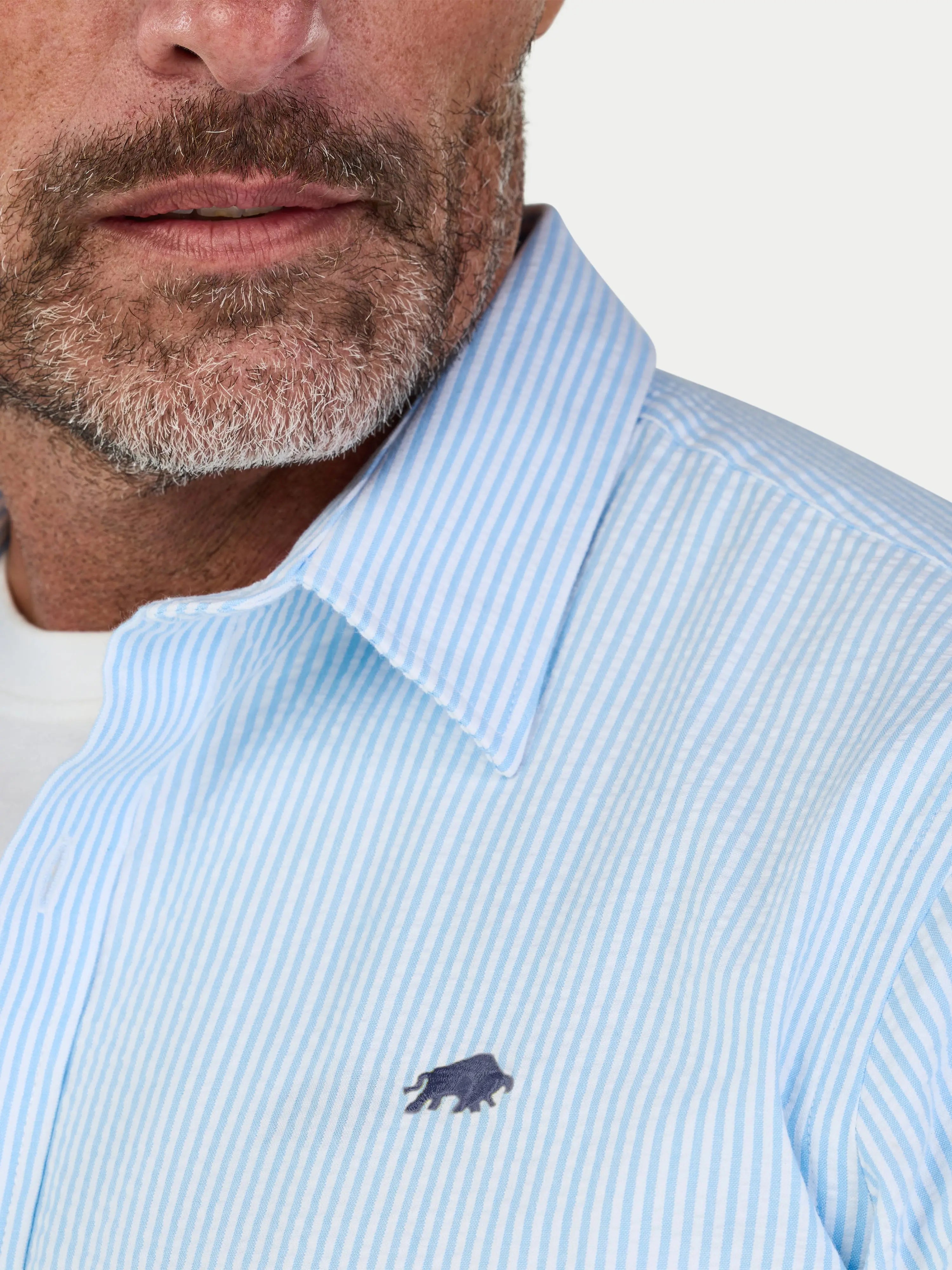 Close-up of a man wearing a Raging Bull short sleeve Orleans Seersucker stripe shirt in sky blue, front detail. 
