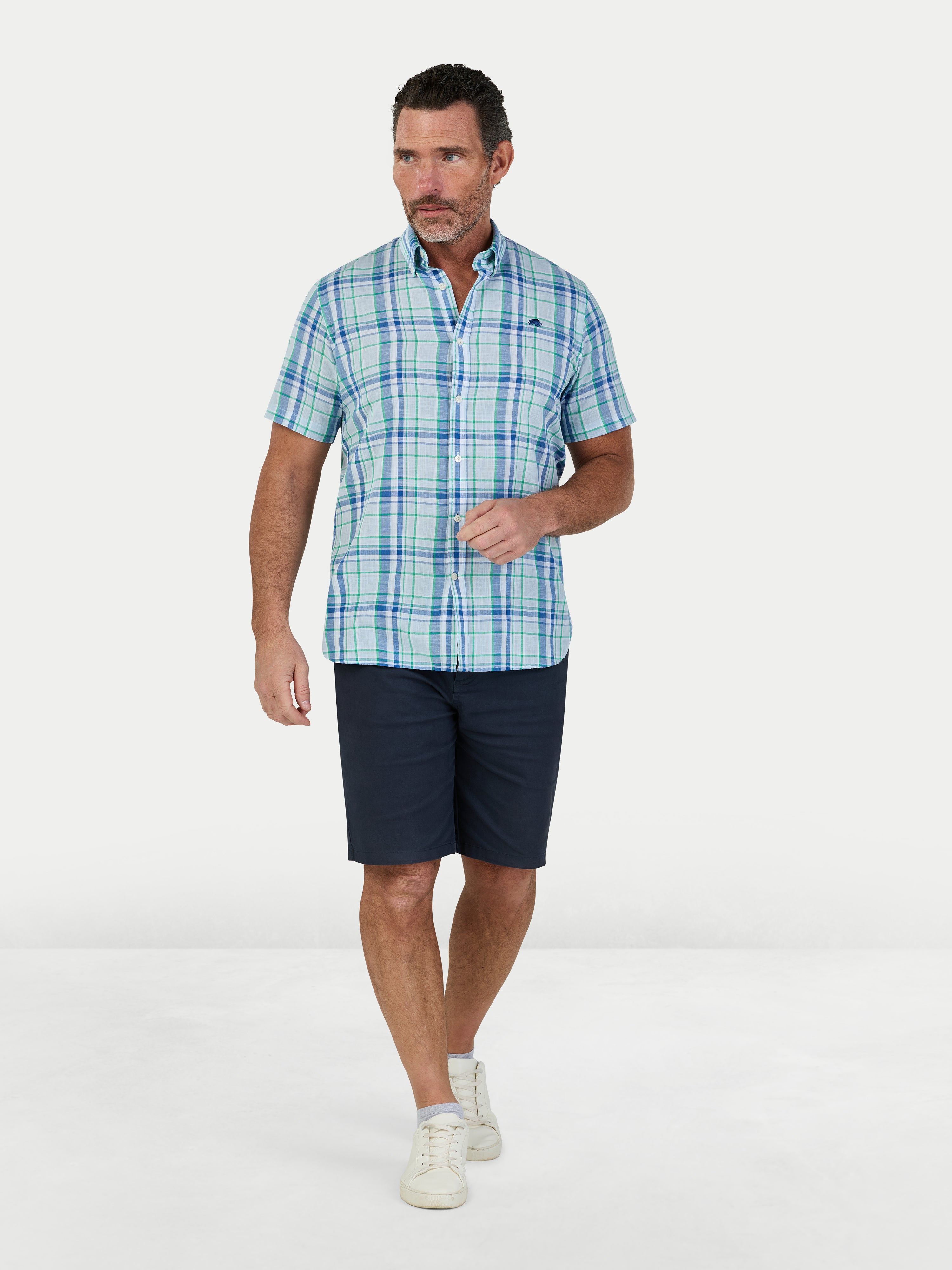 Man wearing a blue plaid shirt and navy shorts on a white background