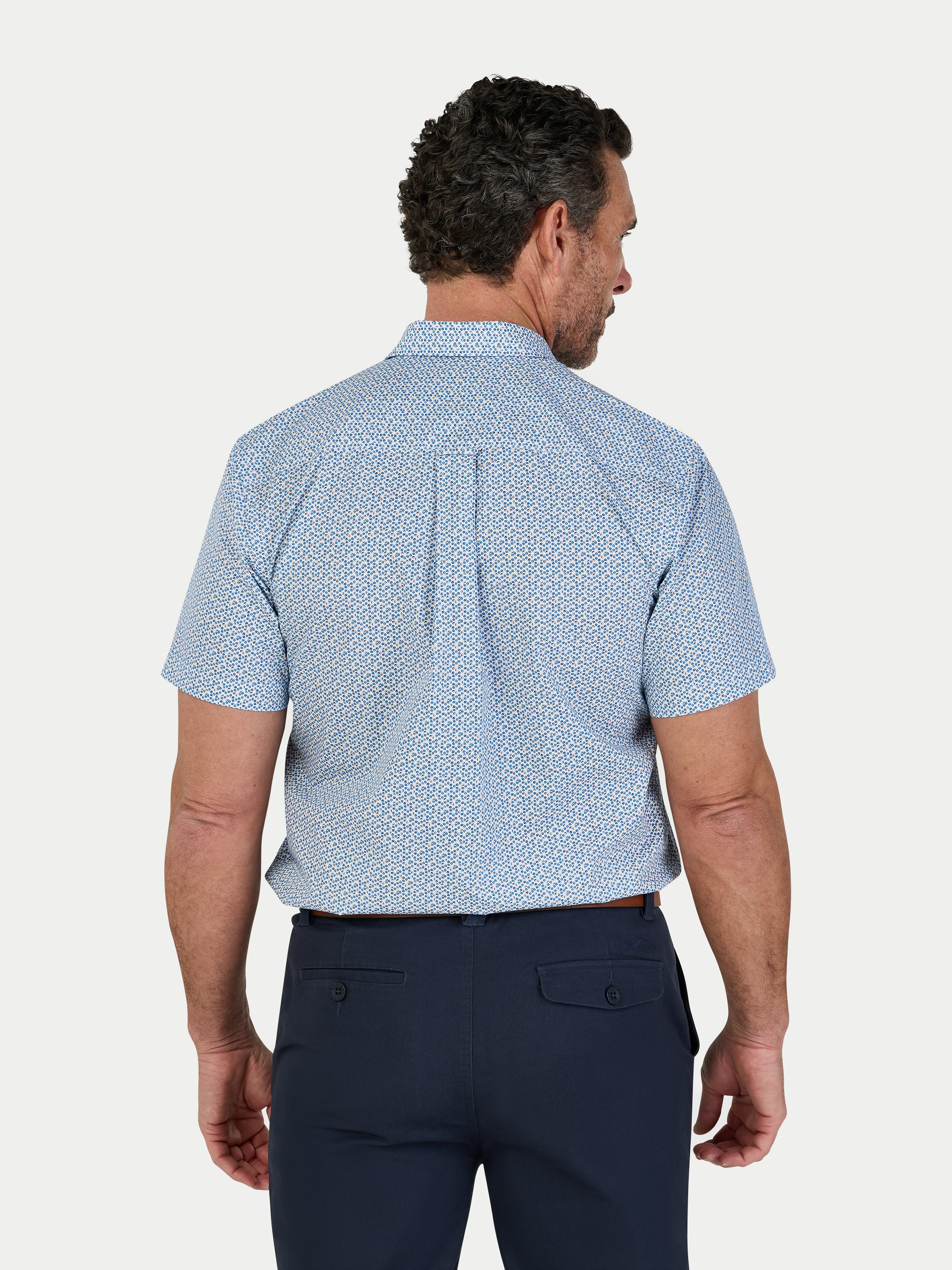 Man wearing a blue patterned shirt and navy pants on a white background