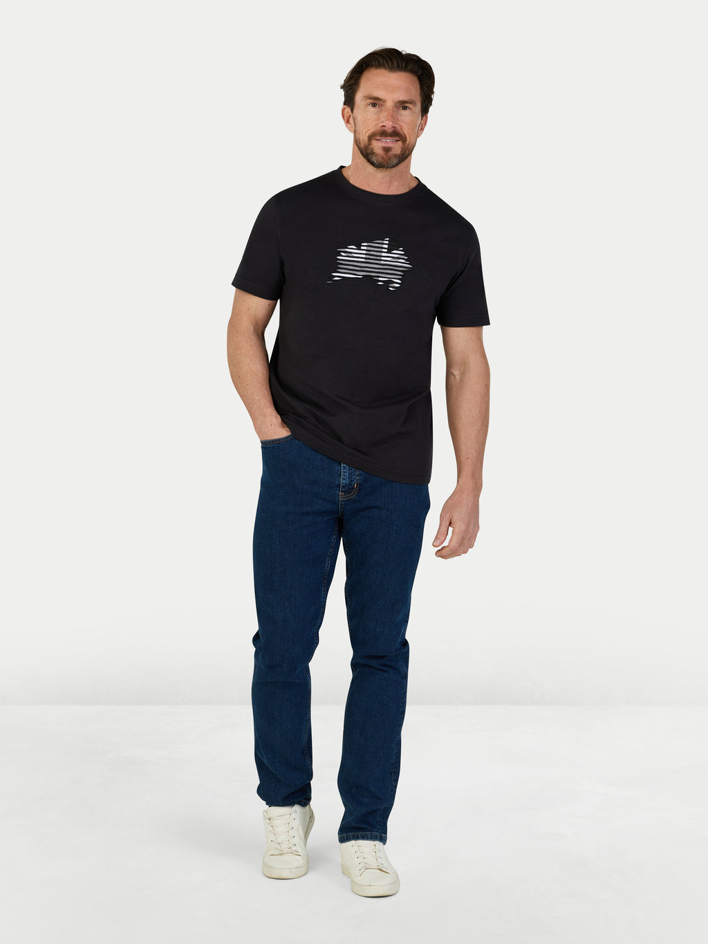 Man wearing a black t-shirt with a logo and blue jeans on a white background