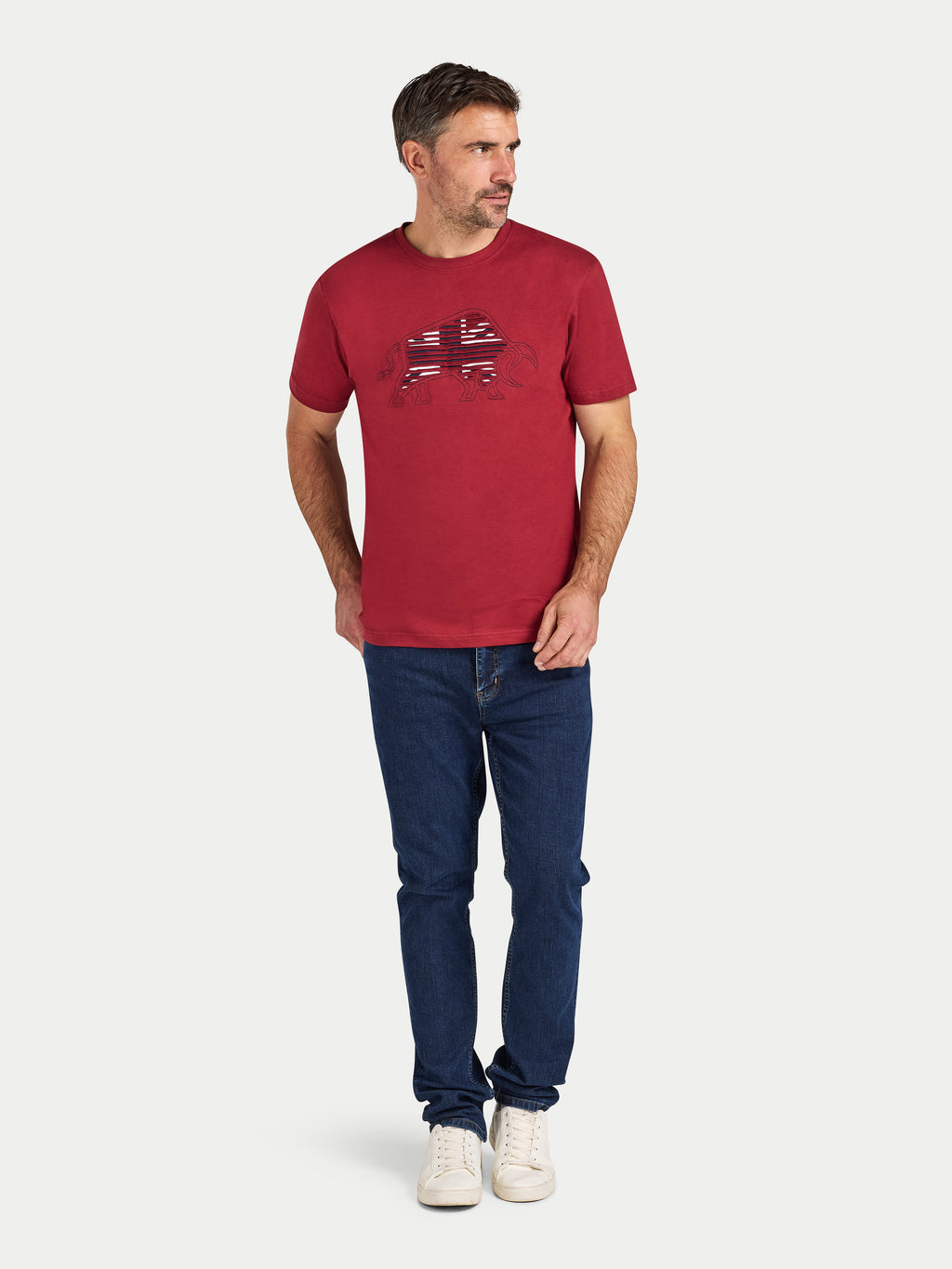 Man wearing a red t-shirt with a logo and blue jeans on a white background