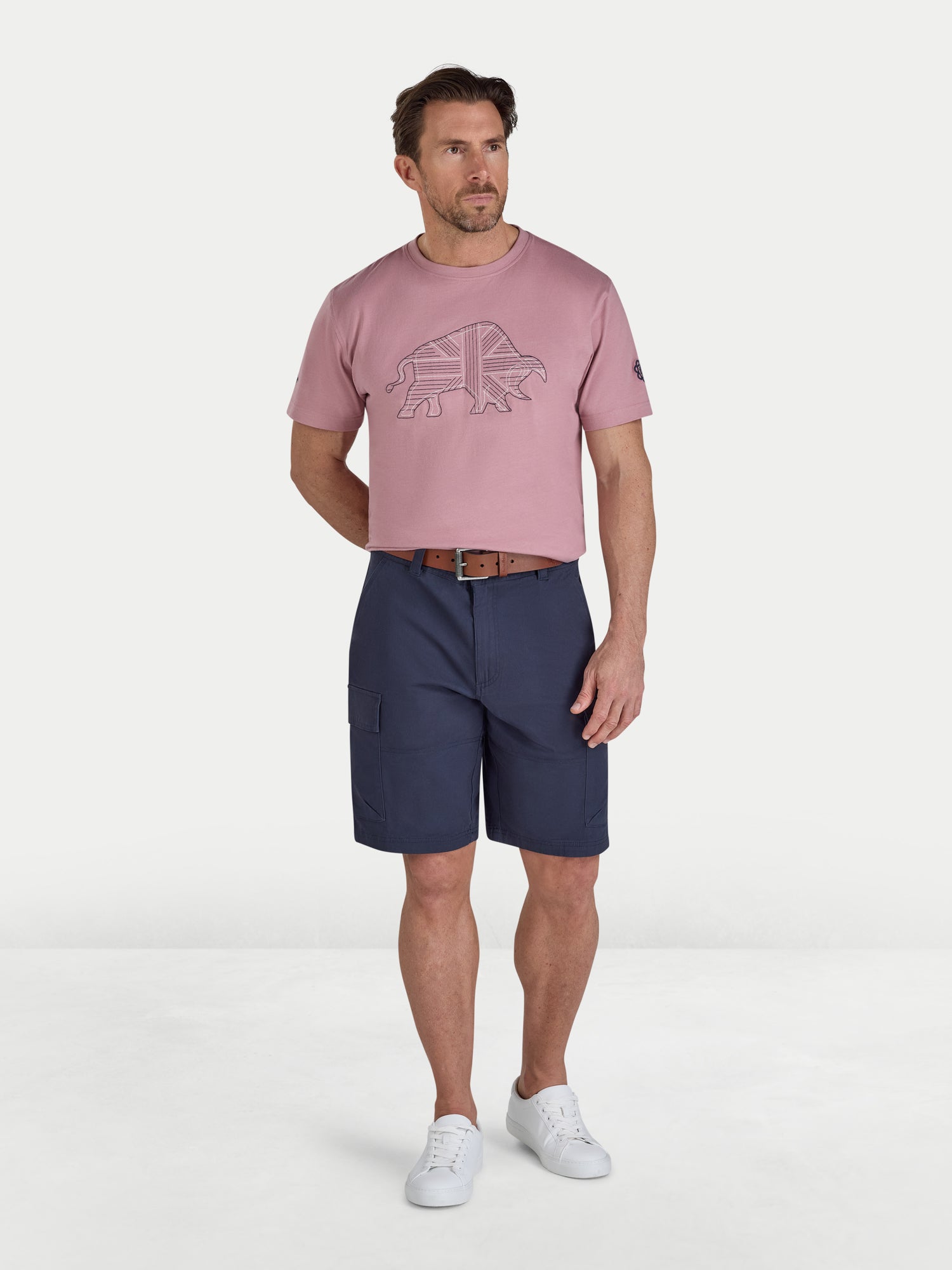 Man wearing a pink t-shirt with a logo and navy shorts on a white background
