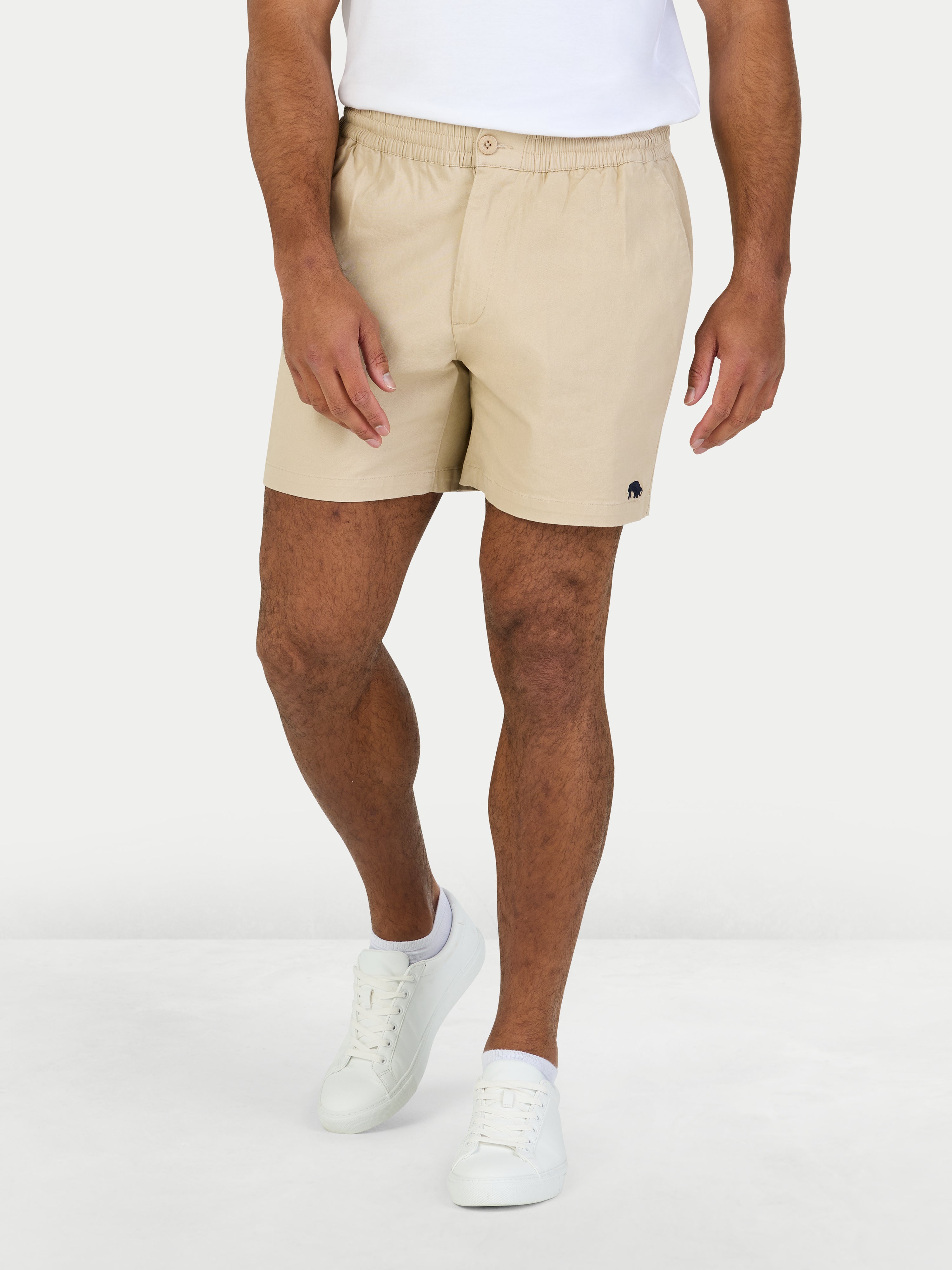 Person wearing beige shorts and white sneakers on a white background