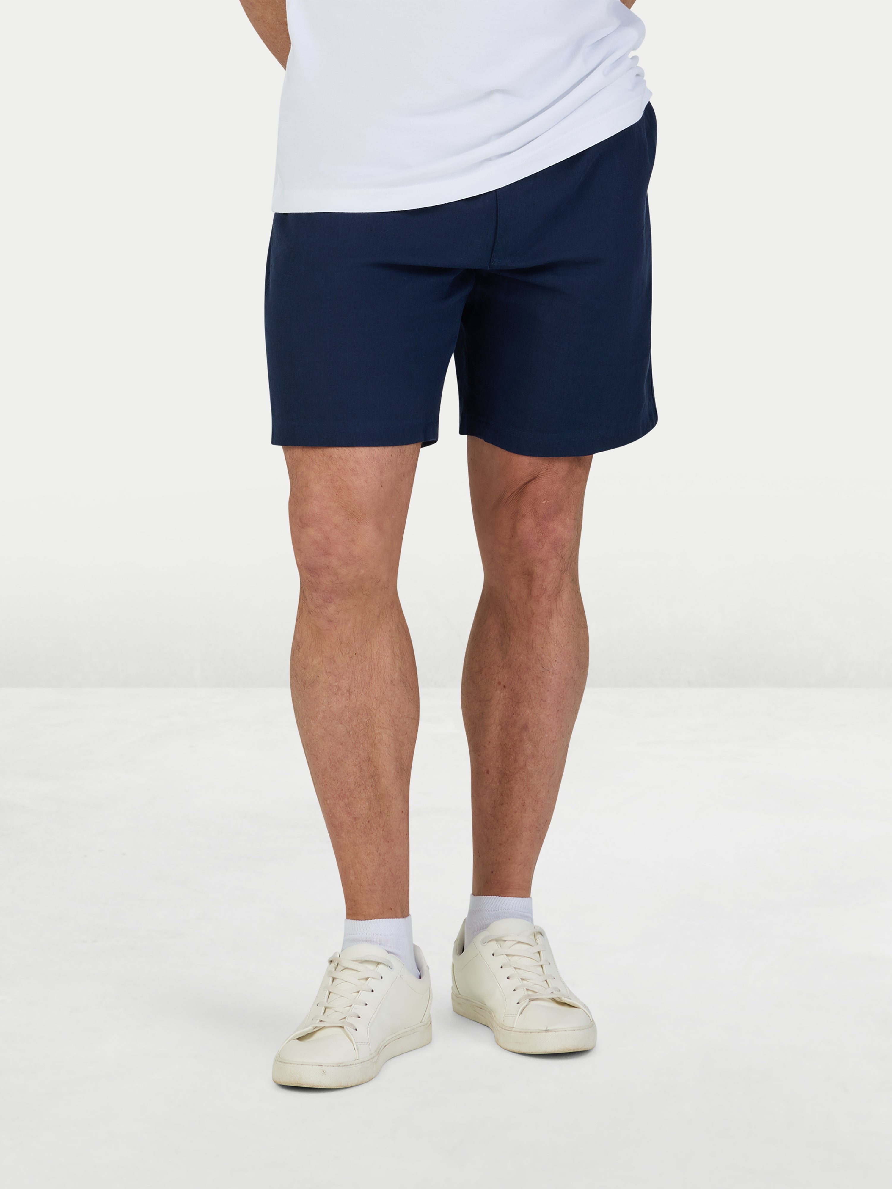 Person wearing navy shorts and white sneakers on a white background