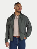 Man wearing a green jacket over a beige shirt with blue jeans on a white background