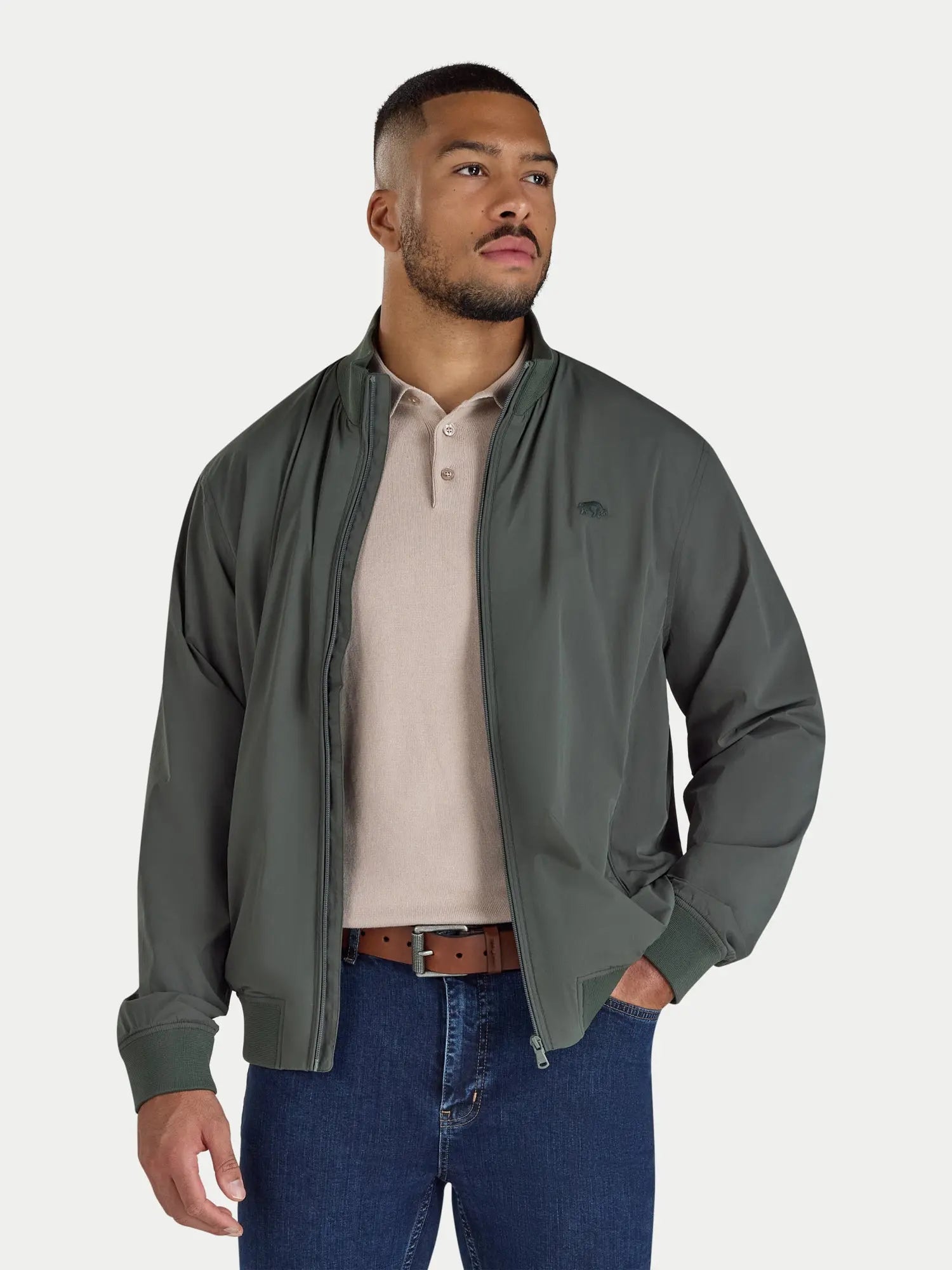 Man wearing a green jacket over a beige shirt with blue jeans on a white background
