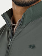 Close-up of a person wearing a green jacket with a brand logo on a light gray background
