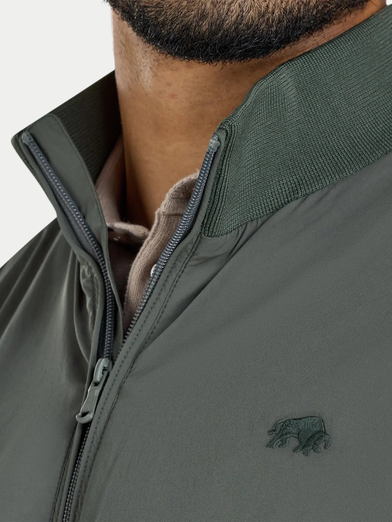 Close-up of a person wearing a green jacket with a brand logo on a light gray background
