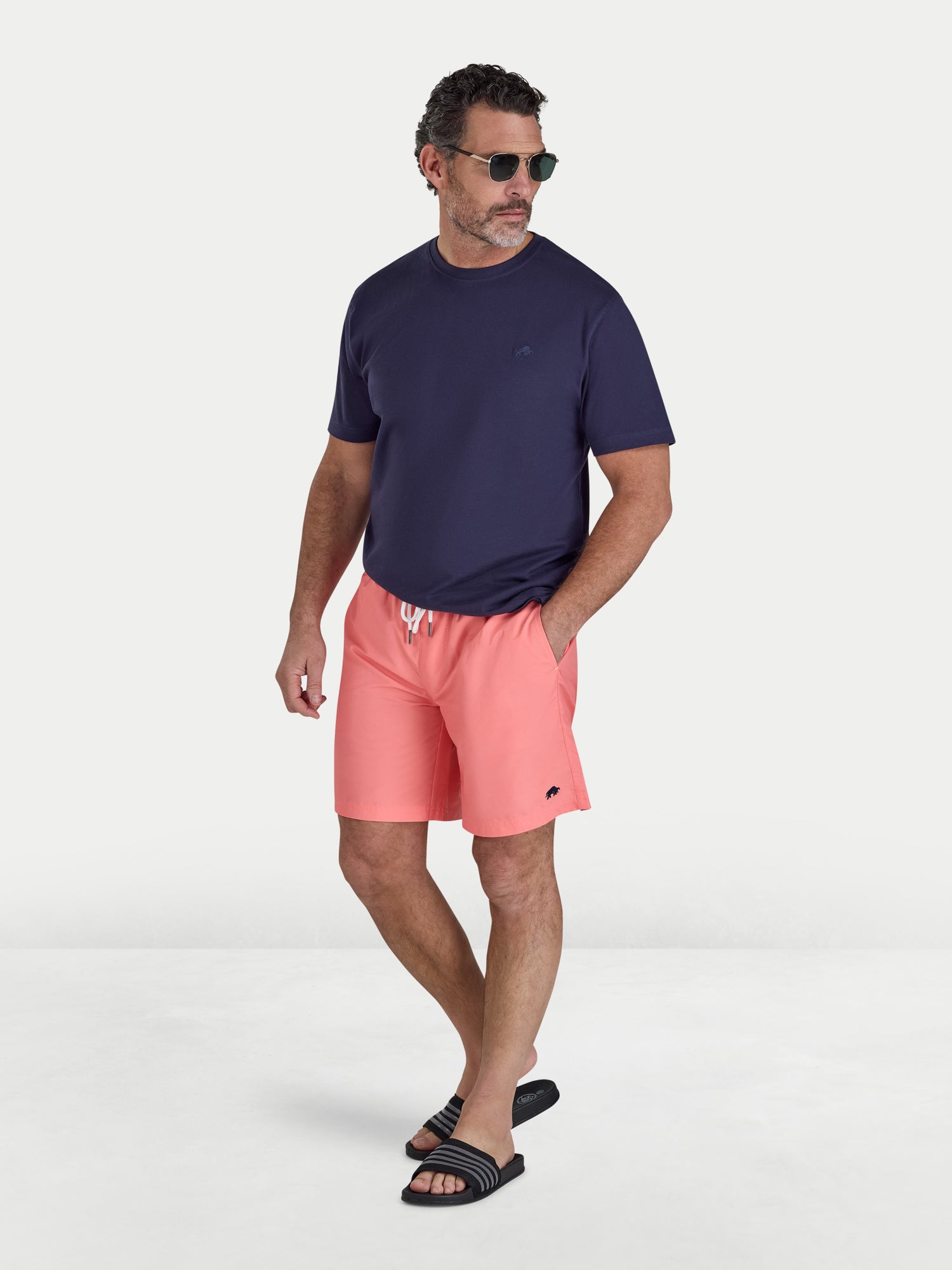 Man wearing a navy t-shirt and pink shorts on a white background