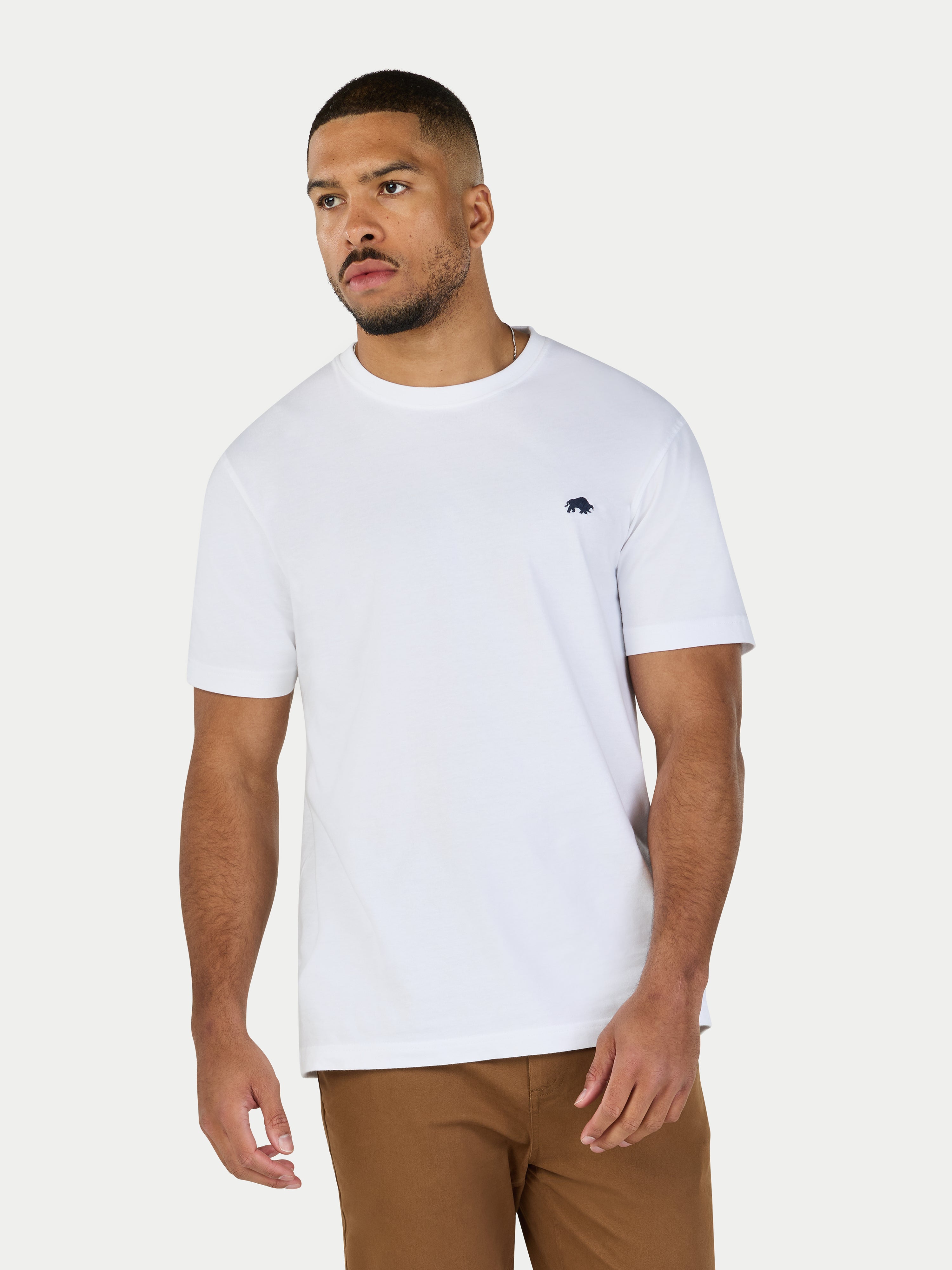 Man wearing a white t-shirt with a small logo on a plain background
