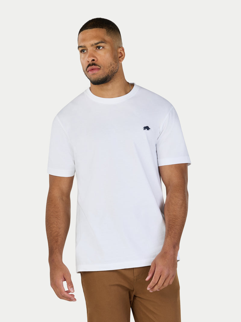 Man wearing a white t-shirt with a small logo on a plain background