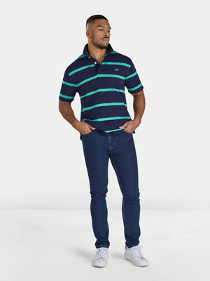 Man wearing a navy and green striped polo shirt with blue jeans on a white background