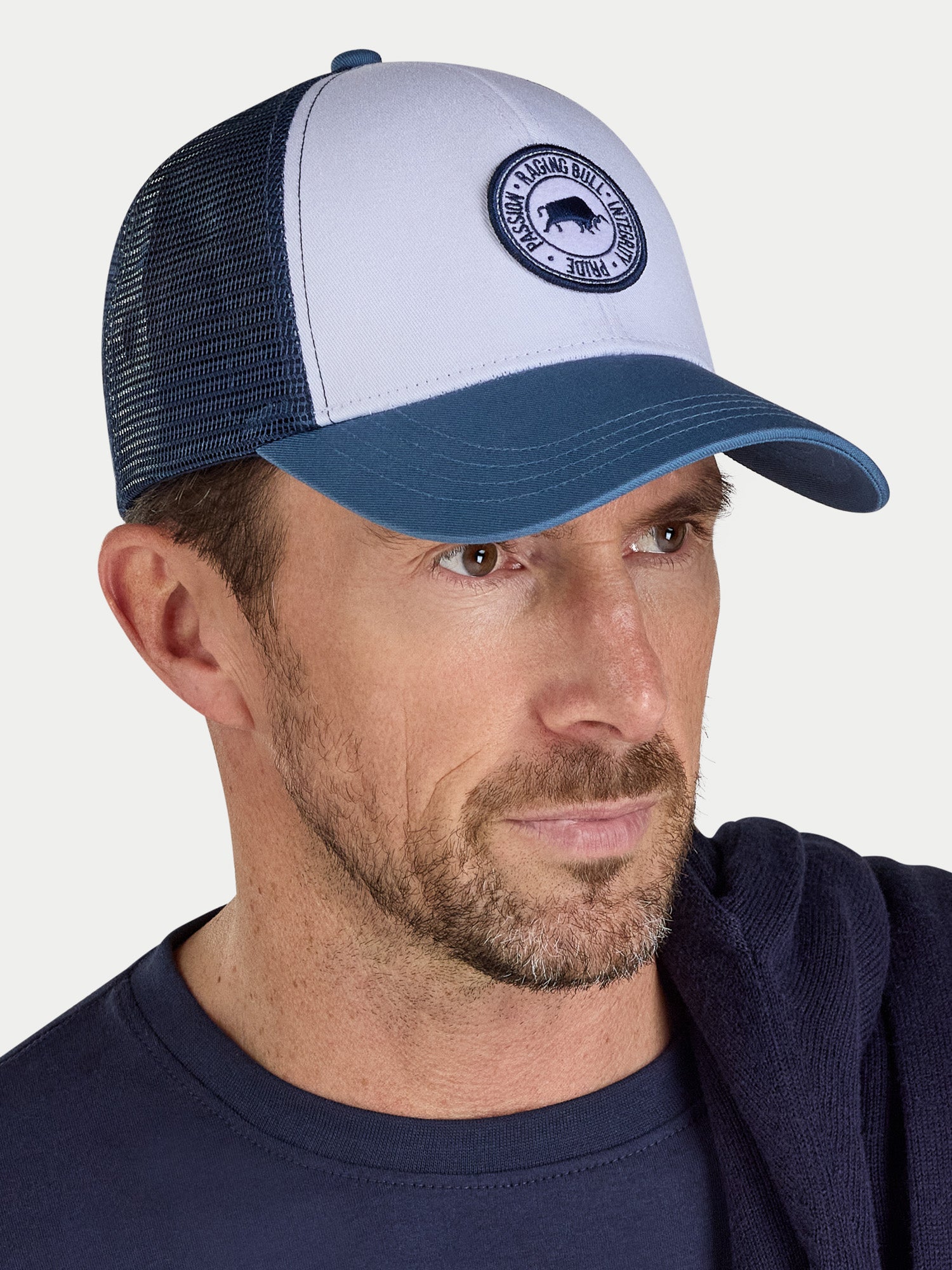 Man wearing a blue and white cap with a logo on a gray background
