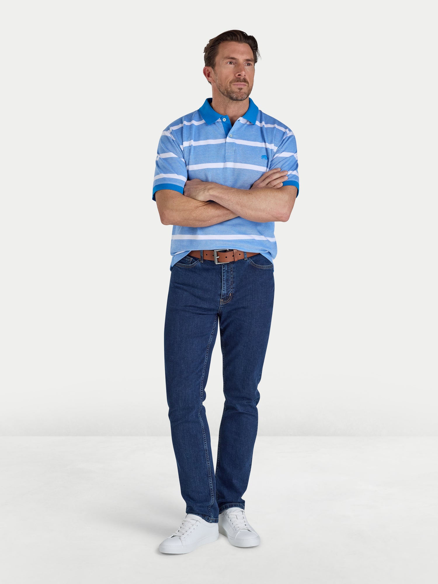 Man wearing a blue striped polo shirt and jeans standing against a white background