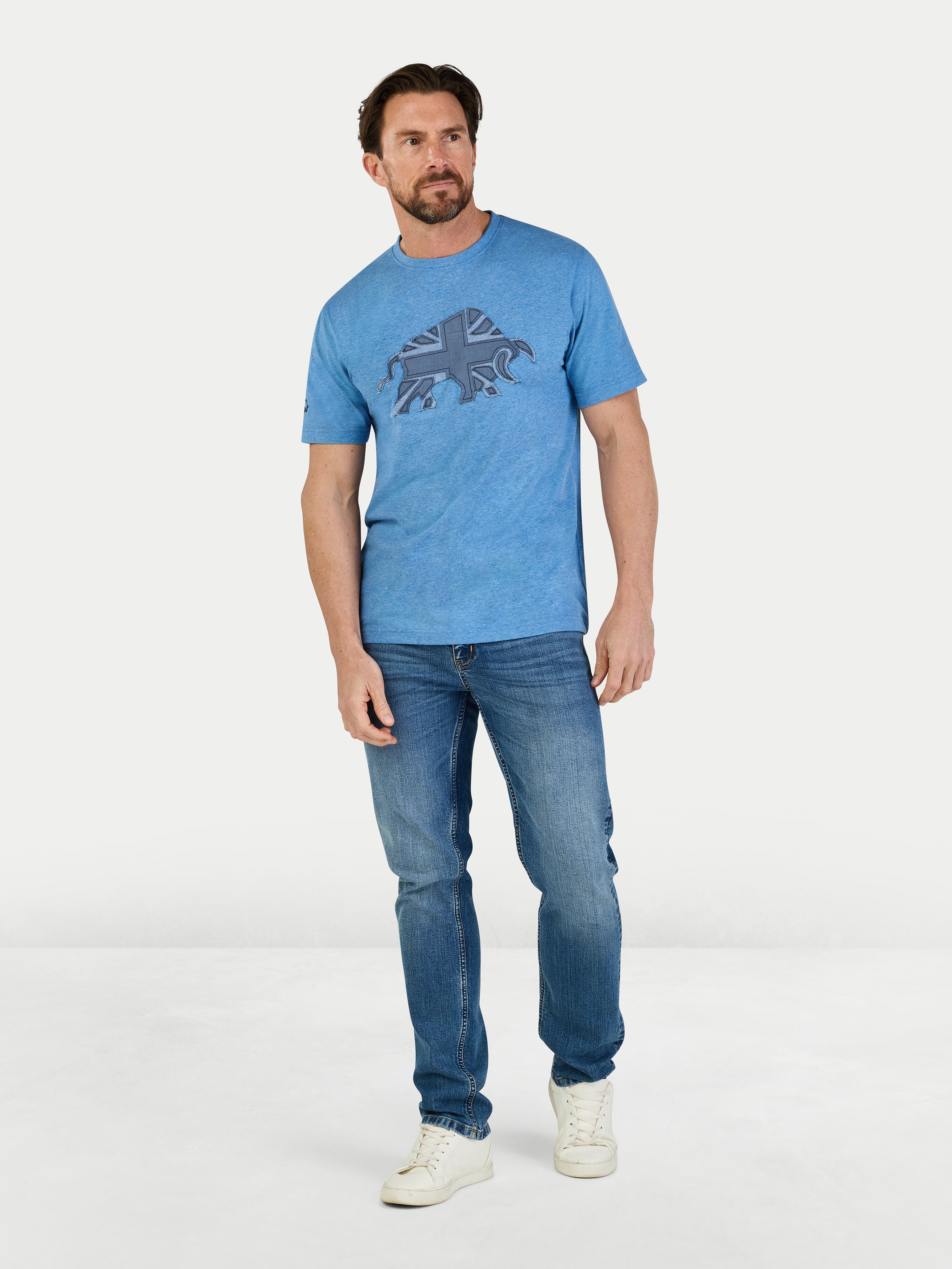 Man wearing a blue t-shirt with a graphic design and jeans on a white background